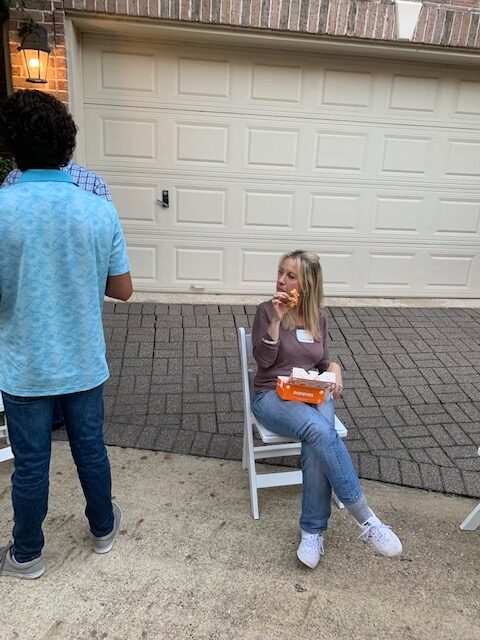 A person sitting on a white wooden chair in front of a garage door carrying a takeout box of Popeyes
