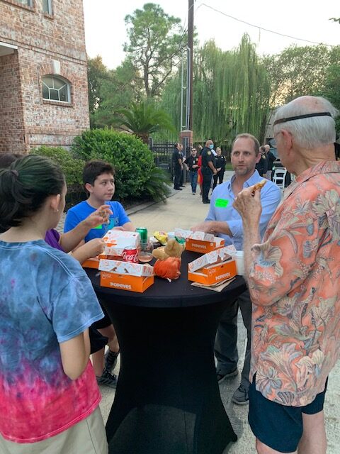 Four people standing and eating Popeyes near a cocktail party table